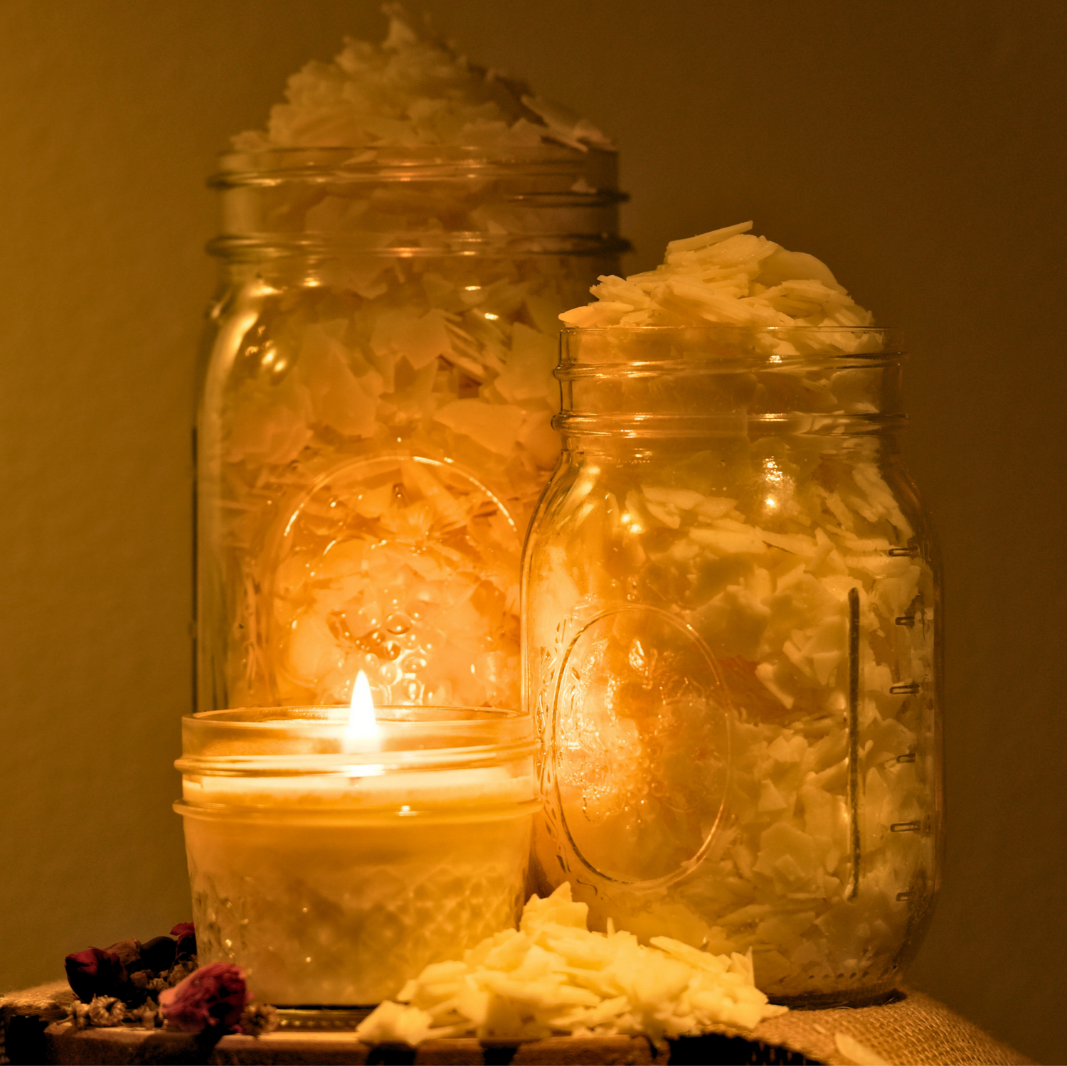 Two glass jars with candle wax inside, surrounded by decorative elements and finished complete candle on a wooden surface.