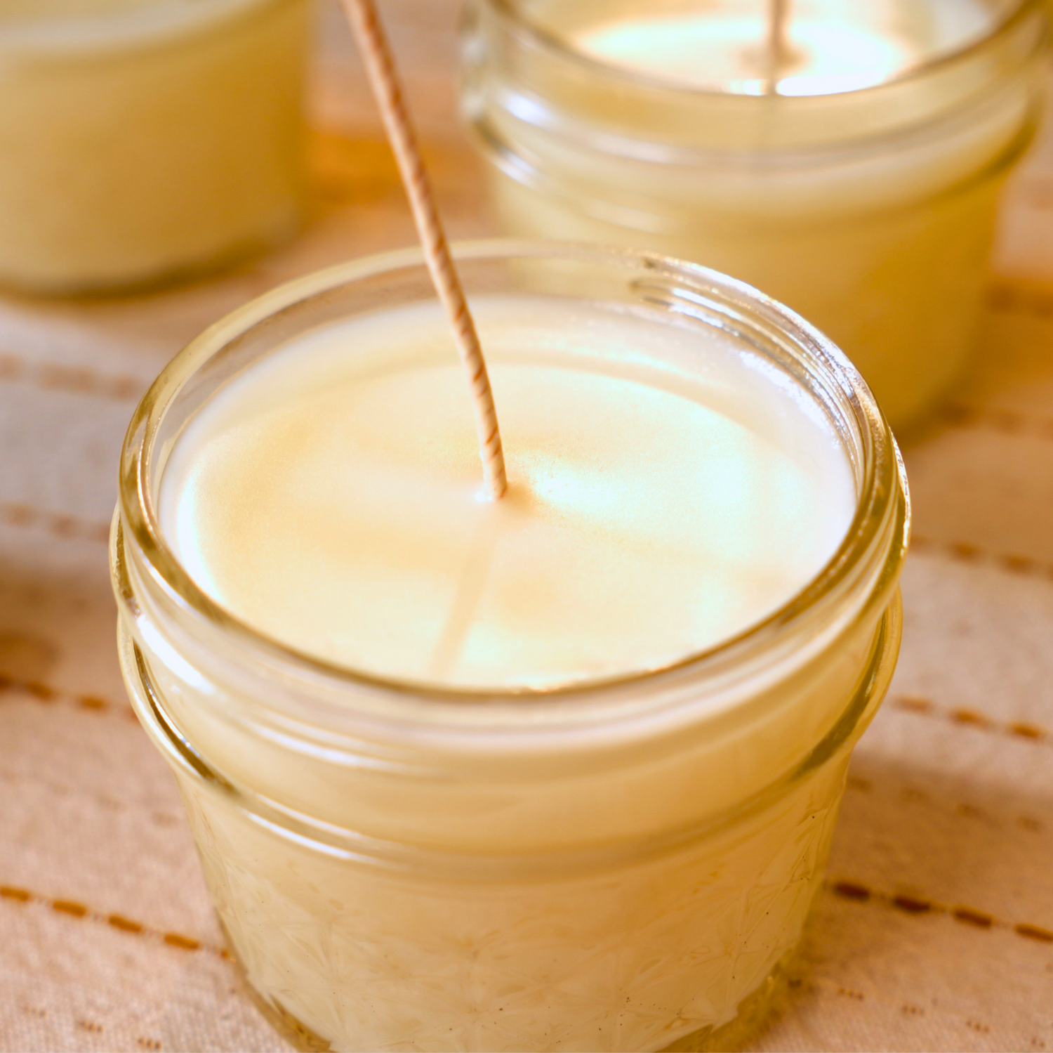 Candle being made in a glass jar on a textured fabric surface