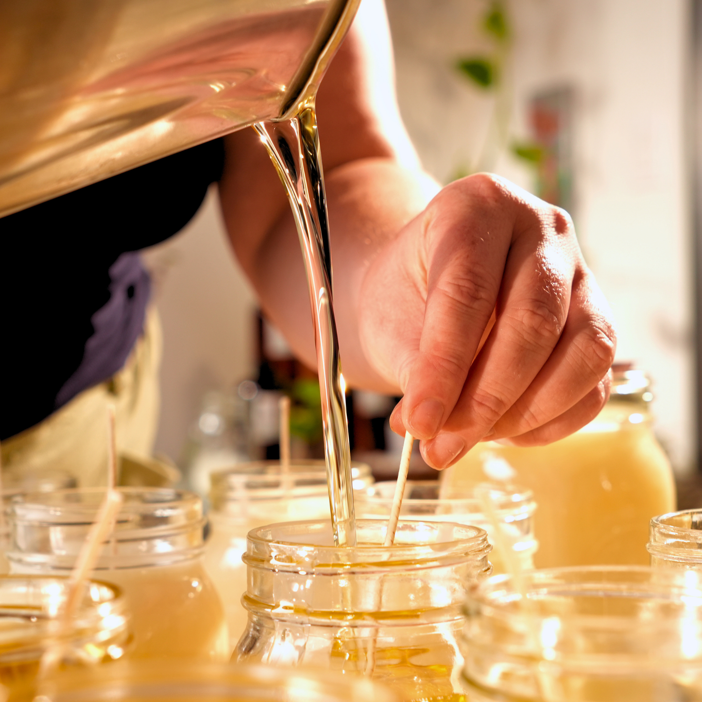 Person pouring a liquid wax into small glass jars.