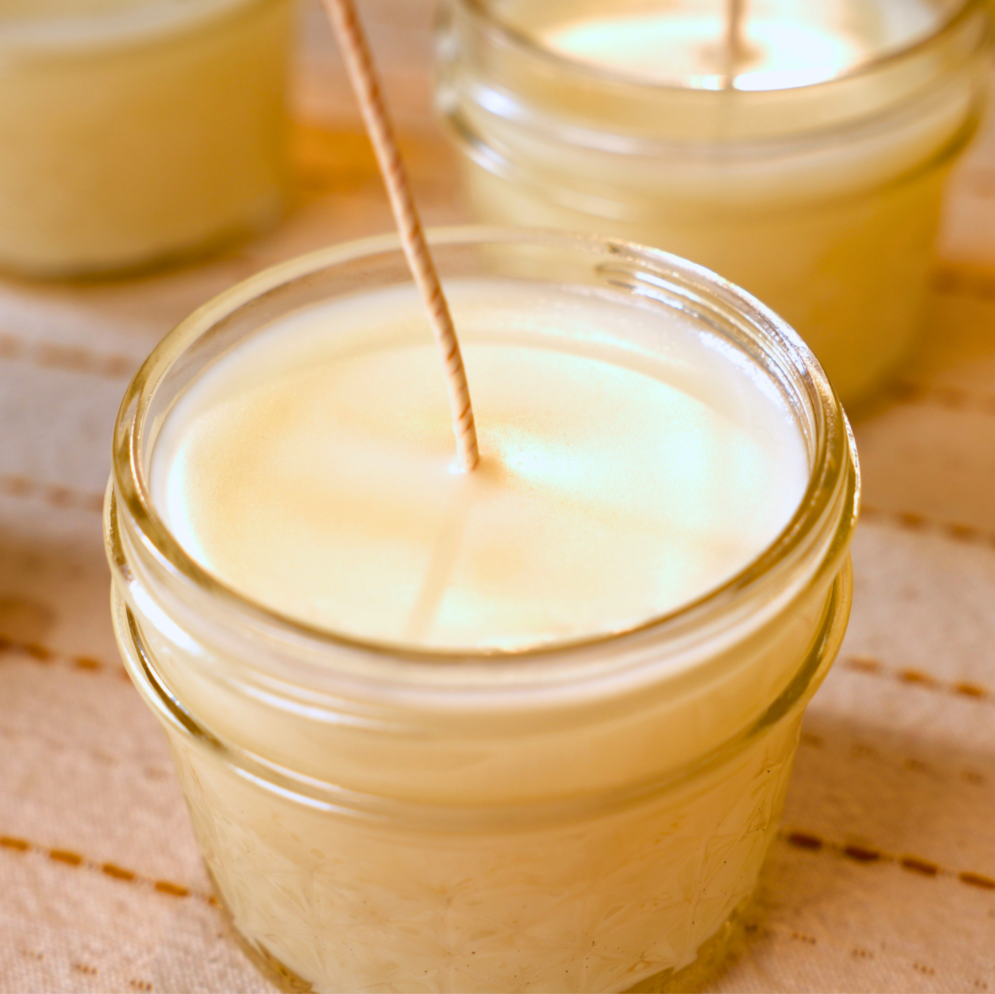 Candle being made in a glass jar on a textured fabric surface