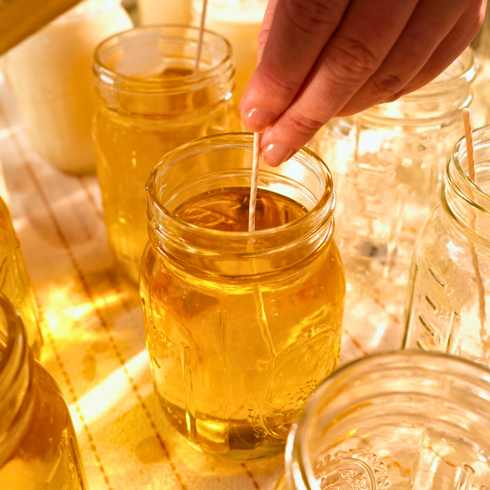 Hand pouring liquid wax into small glass jars on a warm-toned surface.