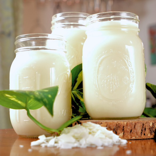 Three glass jars filled with a white finished candles on a wooden surface with green leaves.