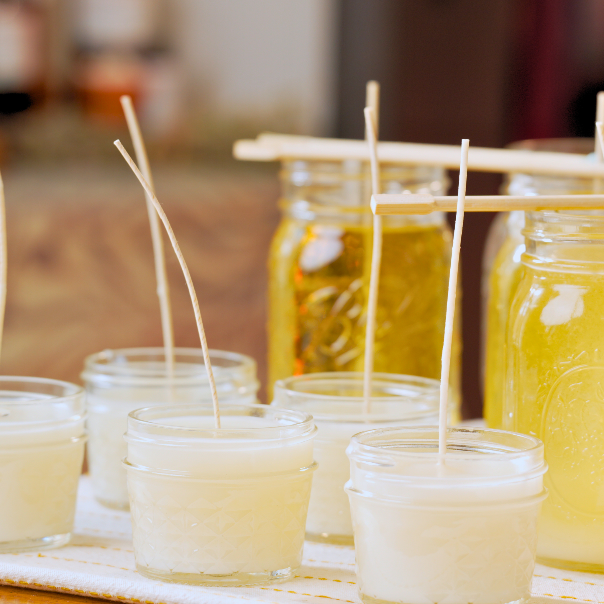 Small cups with wicks and jars of yellow liquid wax on a wooden surface.